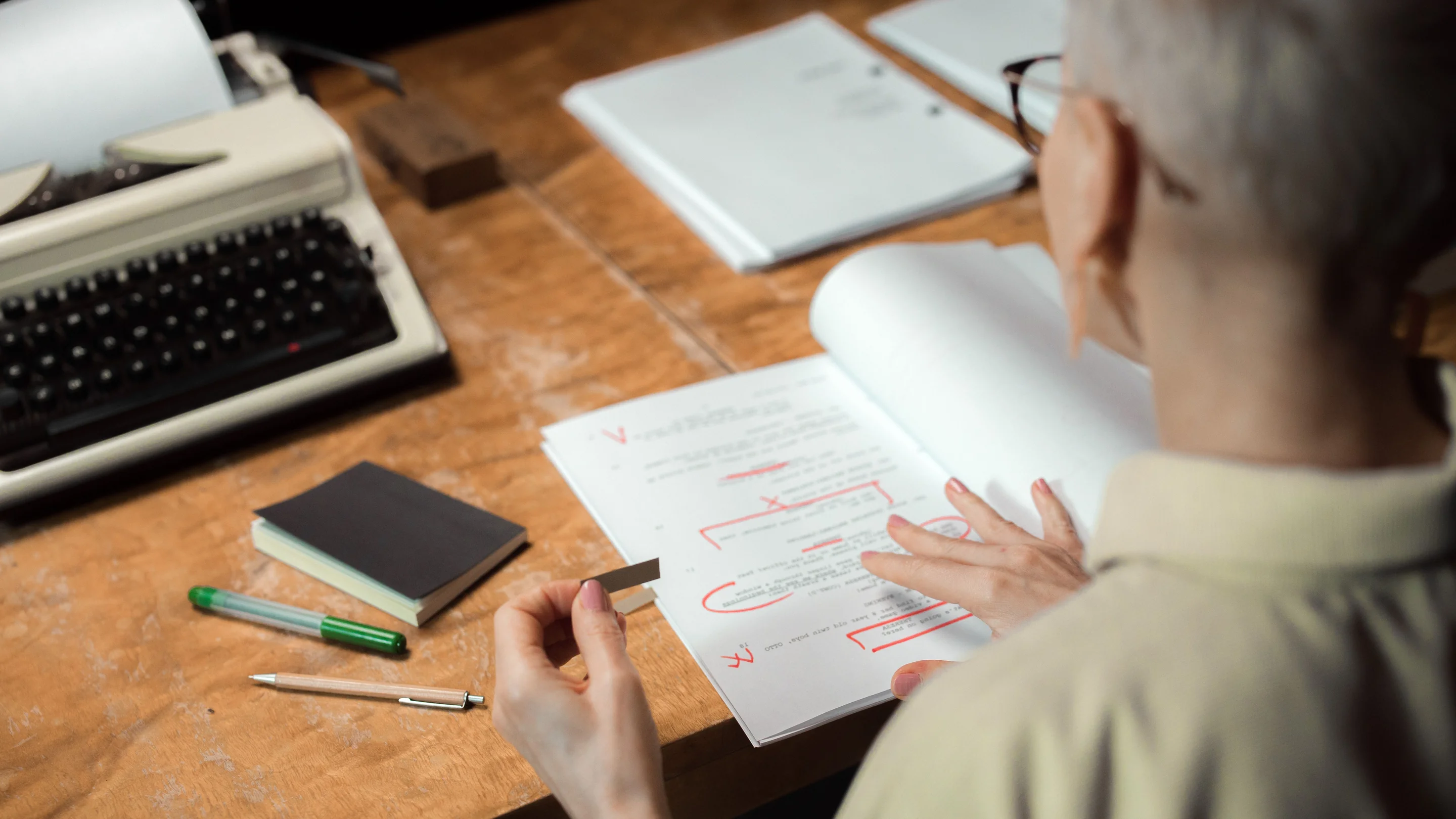 A woman marking an essay with a red pen at a wooden desk.