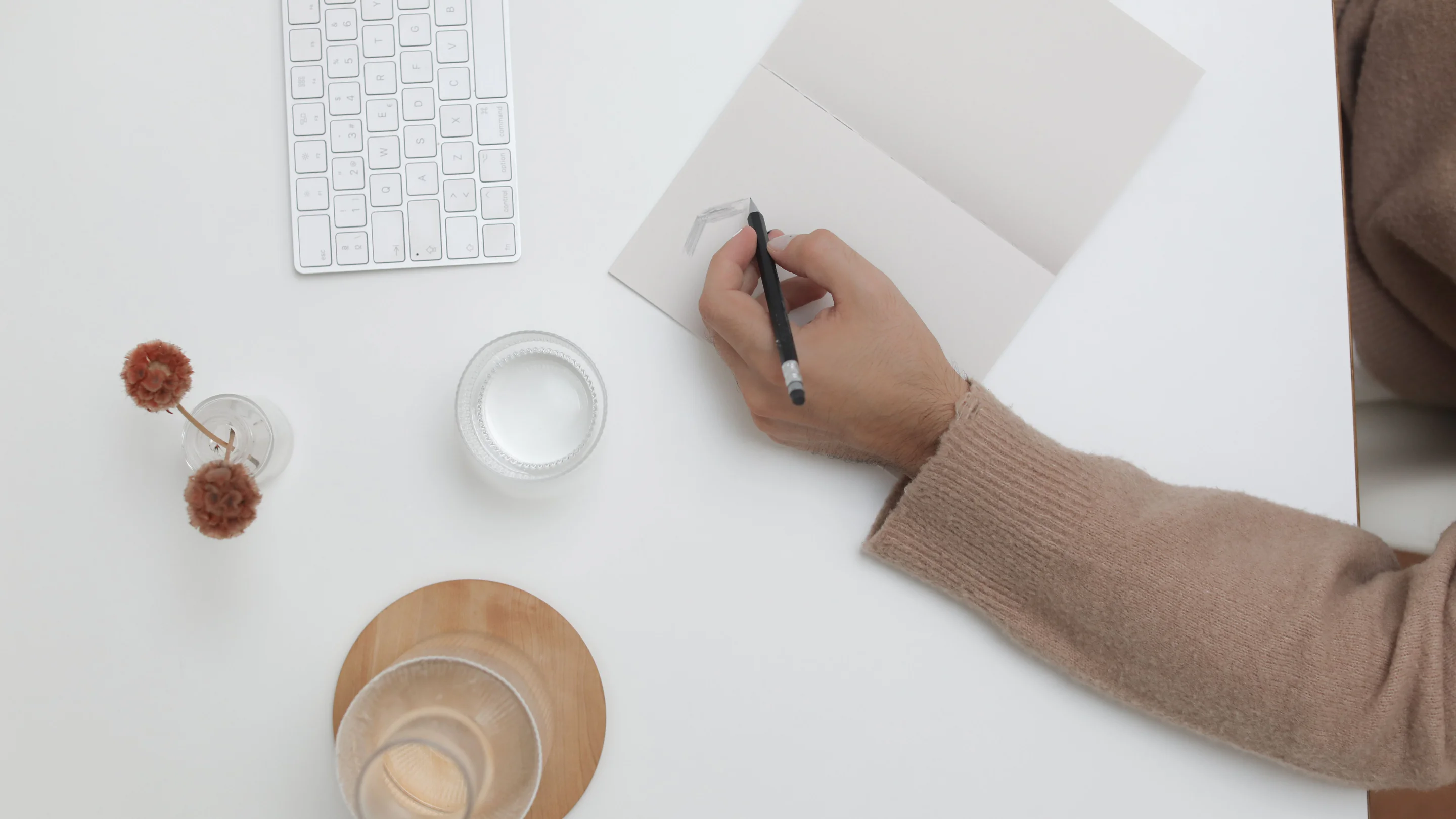 Top view of a clean white desk with a hand writing in a notebook.